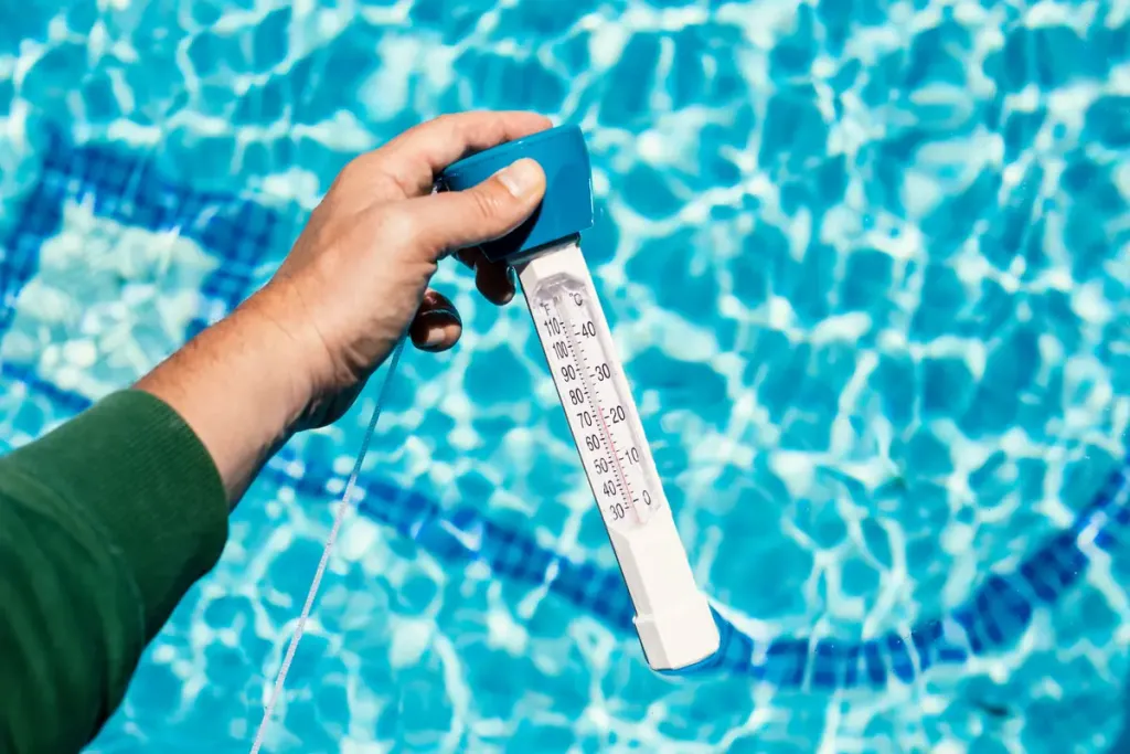 personne tenant un thermomètre au dessus d'une piscine